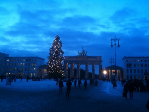 Brandenburg Gate just before nightfall, with a lighted Christmas tree and pedestrians walking by